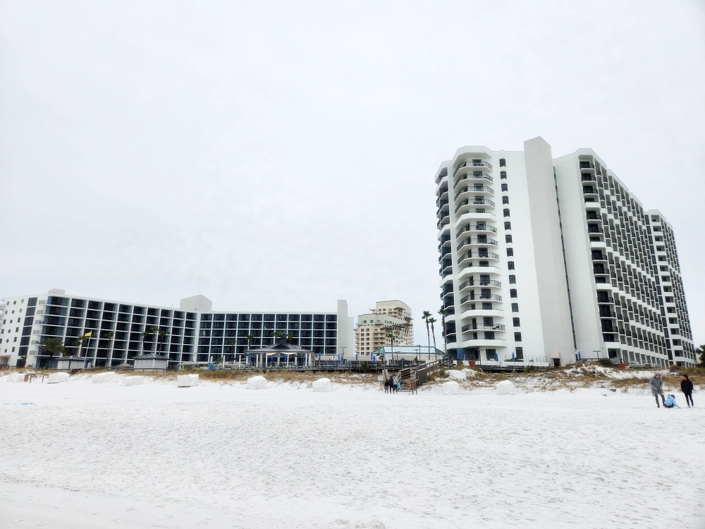 a group of people walking on a snowy beach in front of a building