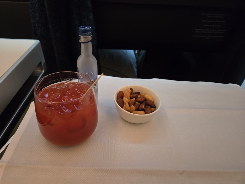 a glass of liquid next to a bowl of nuts and a bottle