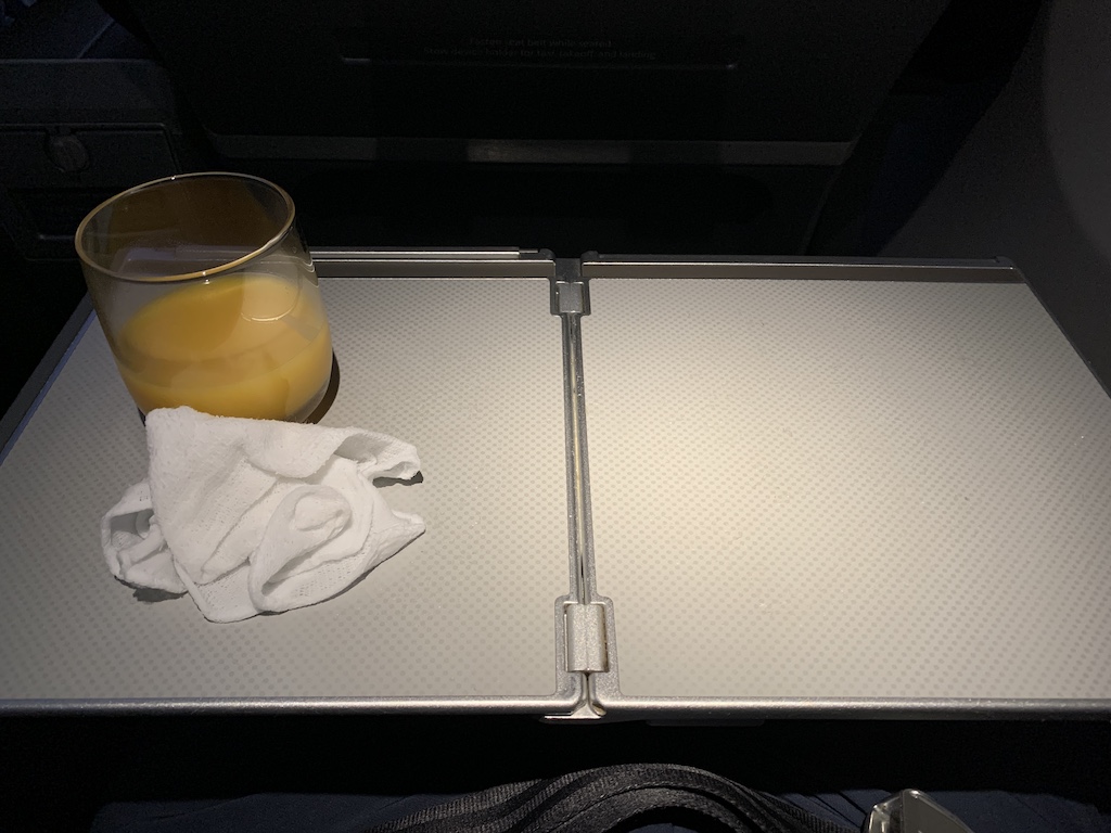 a glass of orange juice on a tray next to a napkin