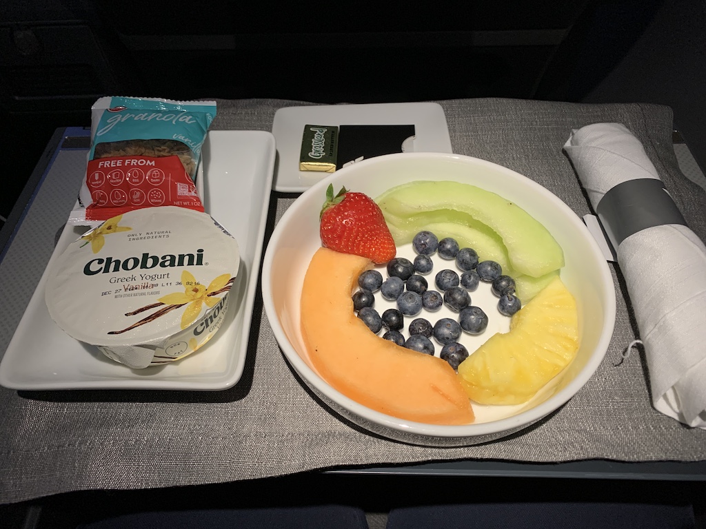 a bowl of fruit and a bag of chips on a tray