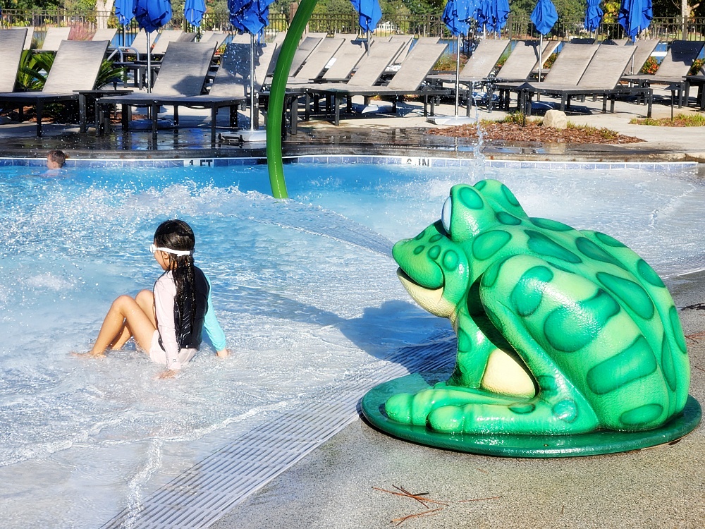 a person sitting in a pool with a large green frog statue