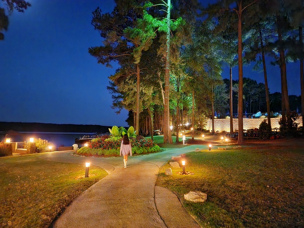 a person walking down a path with trees and lights on either side