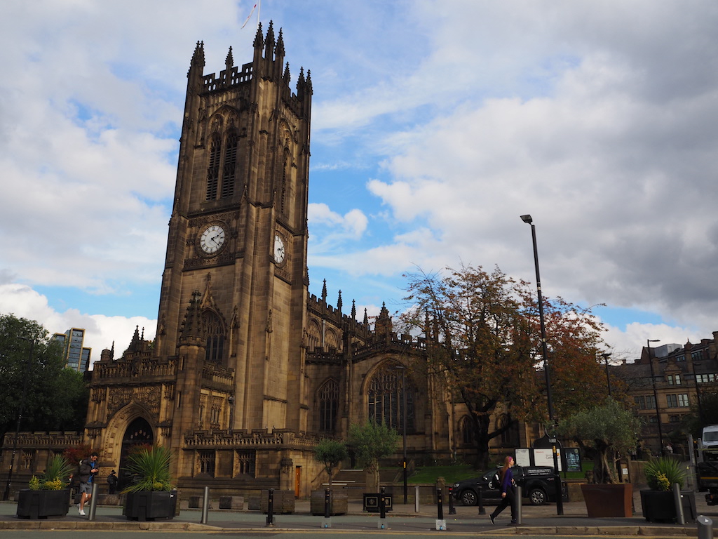 a large building with a clock tower with Manchester Cathedral in the background