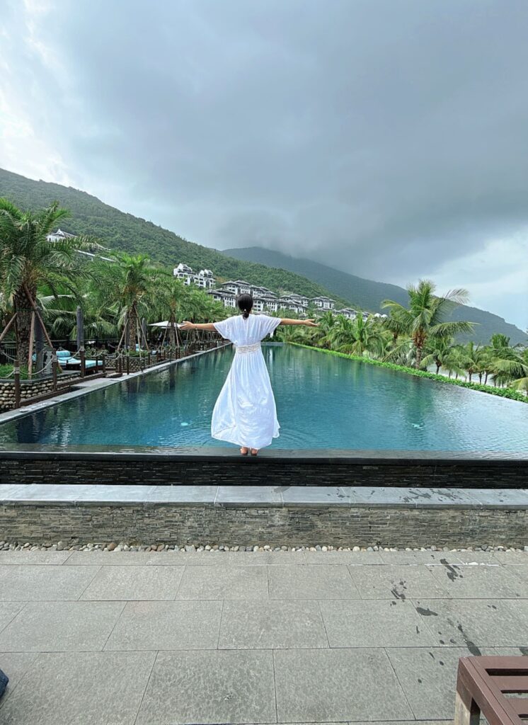 a person in a white dress standing by a pool with a waterfall