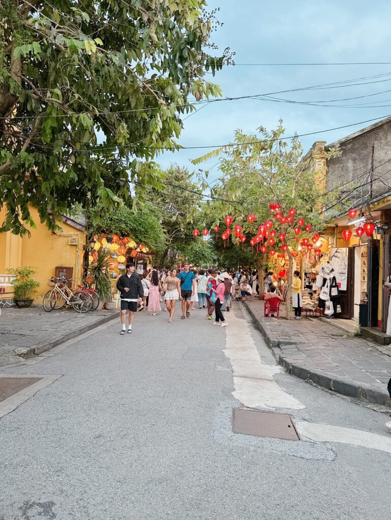 a group of people walking down a street with flowers on the trees