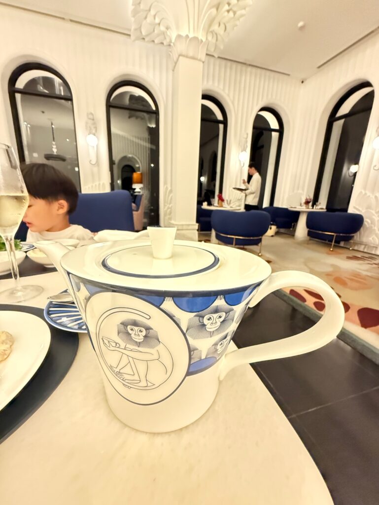 a boy sitting at a table with a teacup and saucer